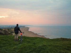 Cyclist facing east towards a rosy sunrise over Hastings from the bicycle path on Galley Hill, near Bexhill-on-Sea, East Sussex