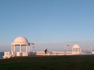 Cycling past the King George V Colonnade on the seafront at Bexhill-on-Sea, East Sussex