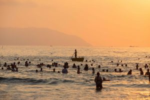 Silhouette of lifeguard standing in a coracle in rich orange glow of sunrise on the beach