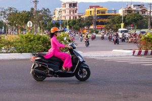 A lady in bright pink drives a motor scooter through evening traffic in Da Nang, Vietnam Photography by Roff Smith