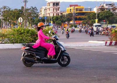 A lady in bright pink drives a motor scooter through evening traffic in Da Nang, Vietnam Photography by Roff Smith